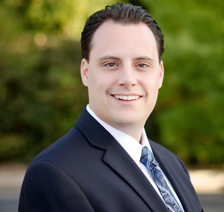 A man in a suit and tie is smiling at the camera with a blurred green background, showcasing the confidence and professionalism you can expect from Georgia Probate Law Group - Your Professional Probate Attorney.